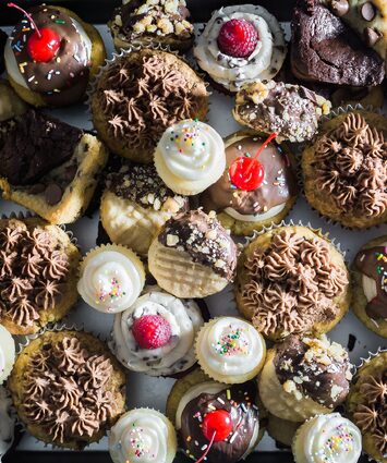 Image of a selection of various cupcakes and muffins with frosting, sprinkles and cherries.